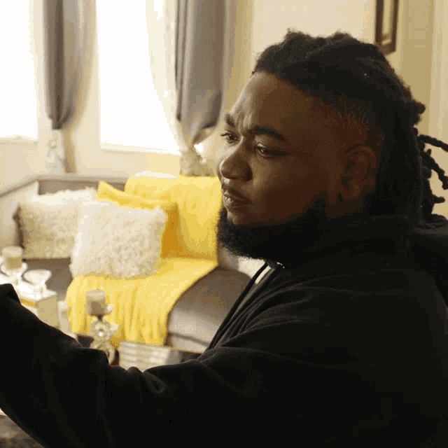 a man with dreadlocks is sitting in front of a couch with a yellow blanket