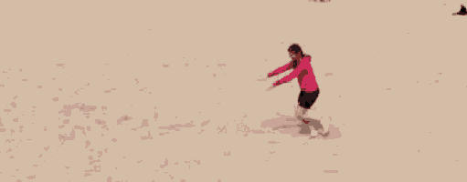 a woman in a pink sweater and shorts is walking on a sandy beach .