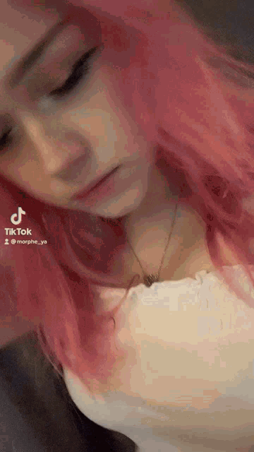 a girl with pink hair is wearing a white shirt and a necklace .