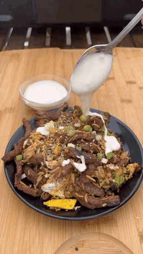 a black plate of food with a spoon pouring sauce on it
