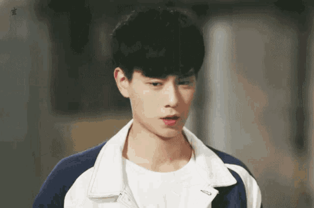 a young man wearing a white t-shirt and a blue and white jacket