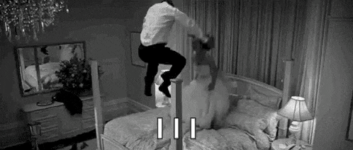 a black and white photo of a man jumping over a bed .
