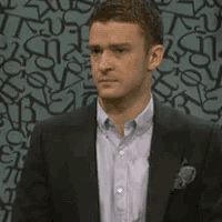 a man in a suit says so in front of a patterned wall