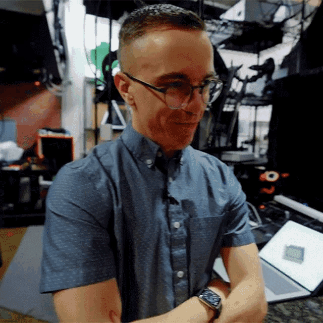 a man wearing glasses and a watch is standing in front of a laptop