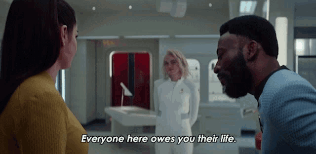 a man talking to two women with the words everyone here owes you their life above him