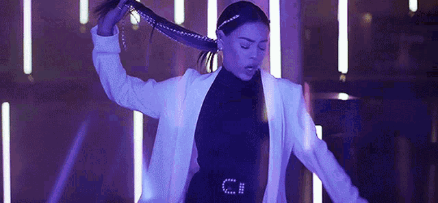 a woman in a white jacket is dancing in a dark room with purple lights .