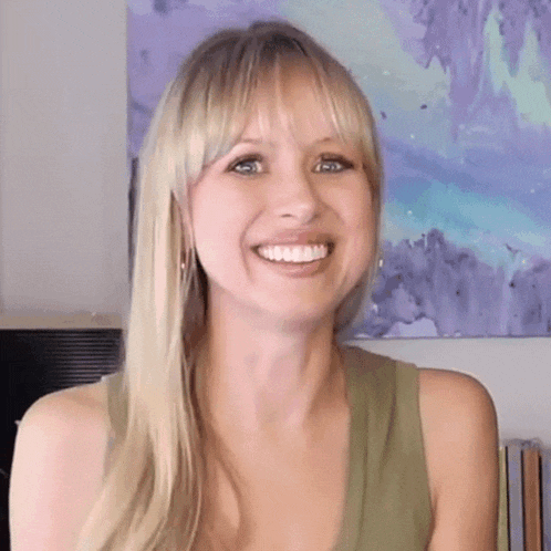 a woman with long blonde hair is smiling in front of a purple painting .