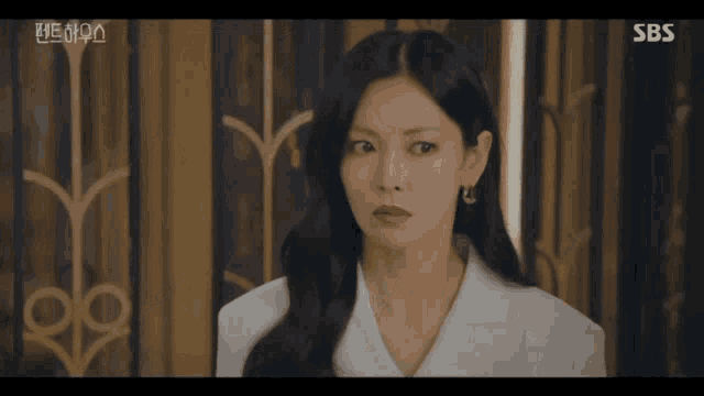a woman in a white suit is standing in front of a wall with sbs written on the bottom