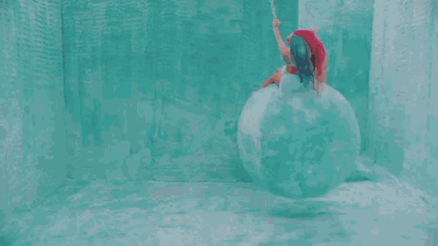 a woman with pink hair is sitting on an ice ball in a room