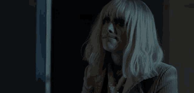 a woman with blonde hair and bangs is sitting in a dark room