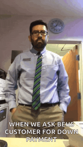 a man in a blue shirt and green tie is standing in front of a clock that says when we ask behs customer for down payment