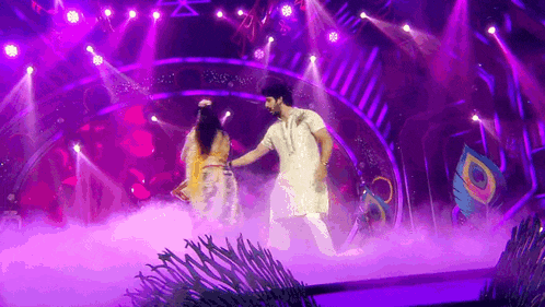 a man and woman are dancing on a stage with purple lights .