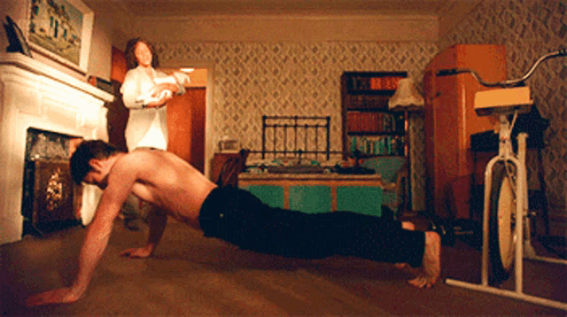 a shirtless man is doing push ups in a living room while a woman holds a baby