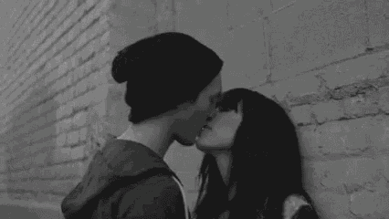 a man and woman are kissing against a brick wall .