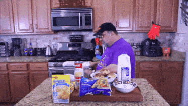 a man in a purple shirt is preparing food in a kitchen with a bag of ruffles