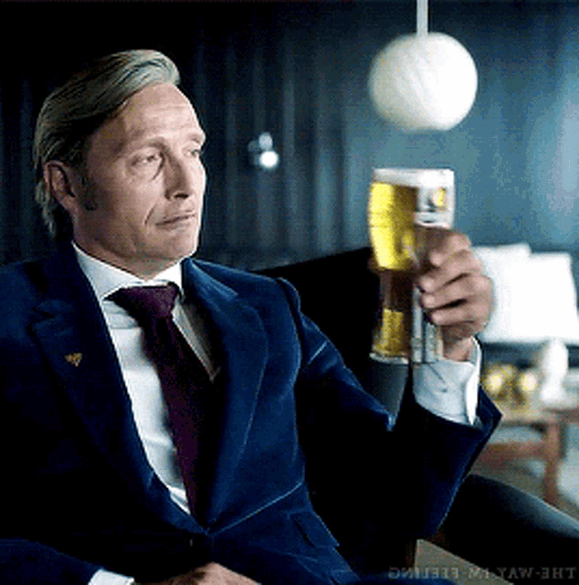 a man in a suit and tie is holding a glass of beer in his hand