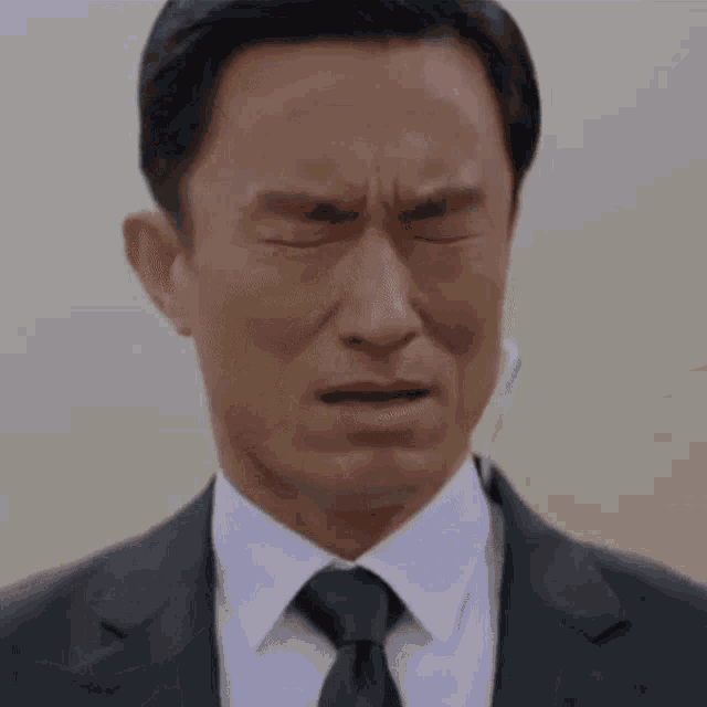 a man in a suit and tie covering his face with his hands .