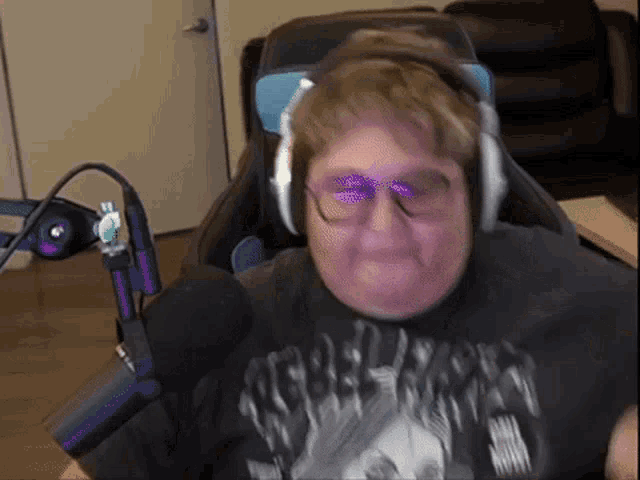 a man wearing headphones and glasses is sitting in front of a microphone and making a face .