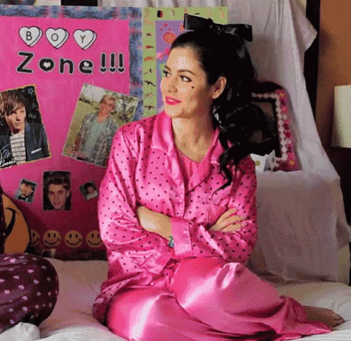 a woman in pink pajamas sits on a bed in front of a poster that says boy zone !!!