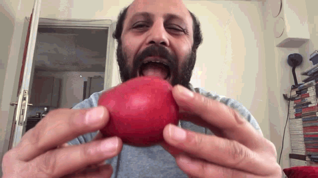 a man with a beard is holding a red apple in his mouth