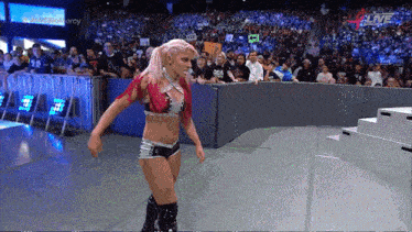 a woman in a wrestling outfit is walking on a stage in front of a crowd with the words live on the screen