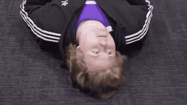 a man in a black adidas jacket is laying on his back and giving a thumbs down sign