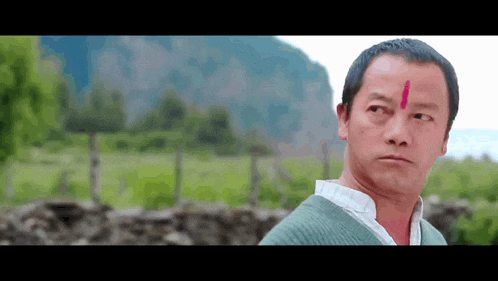 a man with a red circle on his forehead looks at the camera