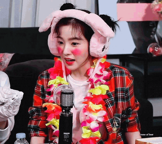 a woman wearing pink bunny ears and a flower lei is sitting in front of a microphone