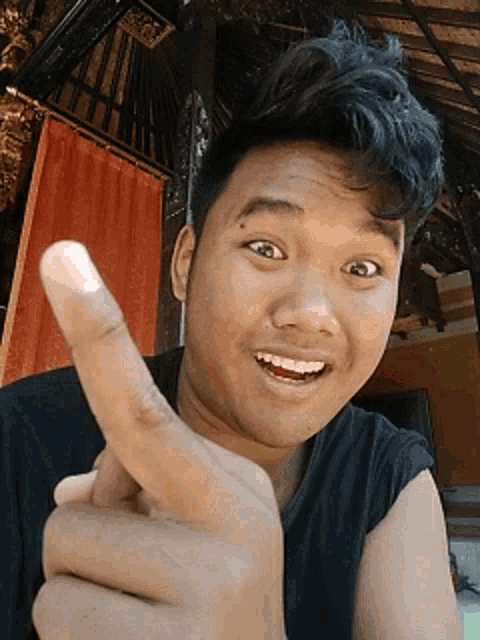 a young man in a black shirt is pointing his finger at the camera