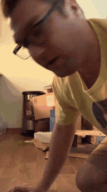 a man wearing glasses and a yellow shirt is kneeling on a wooden floor