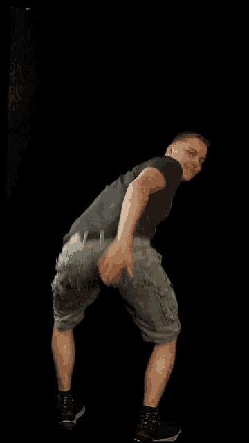 a man wearing shorts and a black shirt is standing in front of a black background
