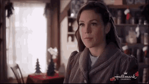 a woman is standing in a room with a christmas tree in the background and looking at the camera .