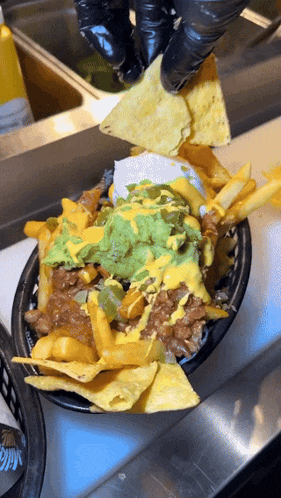 a person wearing black gloves is dipping a tortilla chip into guacamole