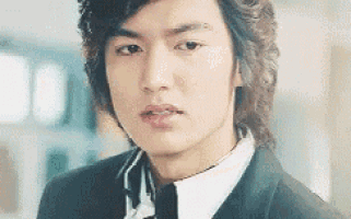 a young man with long hair is wearing a suit and tie and looking at the camera .