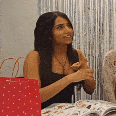 a woman in a black dress is sitting at a table with a magazine and a red bag .