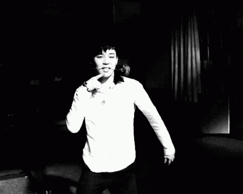 a man in a white shirt is standing in a dark room holding a cigarette in his mouth