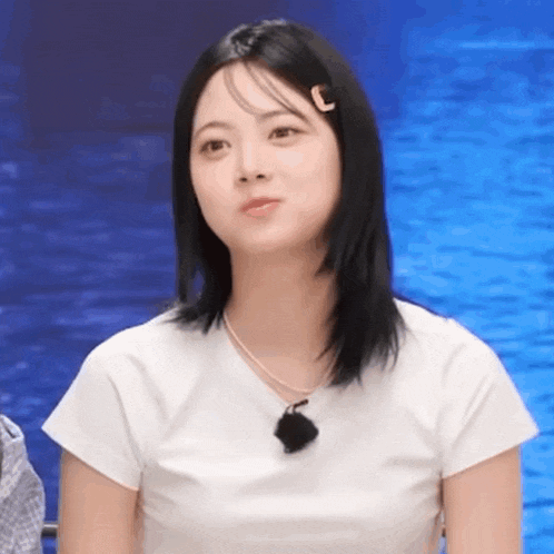 a young woman wearing a white t-shirt and a necklace is sitting in front of a body of water .