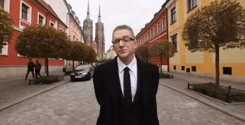 a man in a suit and tie stands in front of a row of colorful buildings