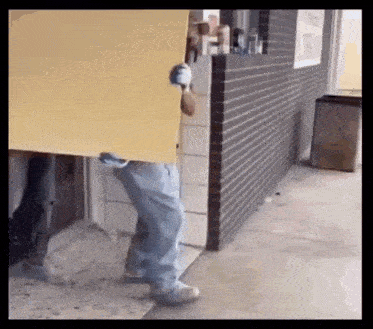 a man is carrying a large piece of cardboard in front of a brick wall .