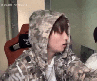 a young man wearing a camouflage jacket with a hood is sitting in a room .