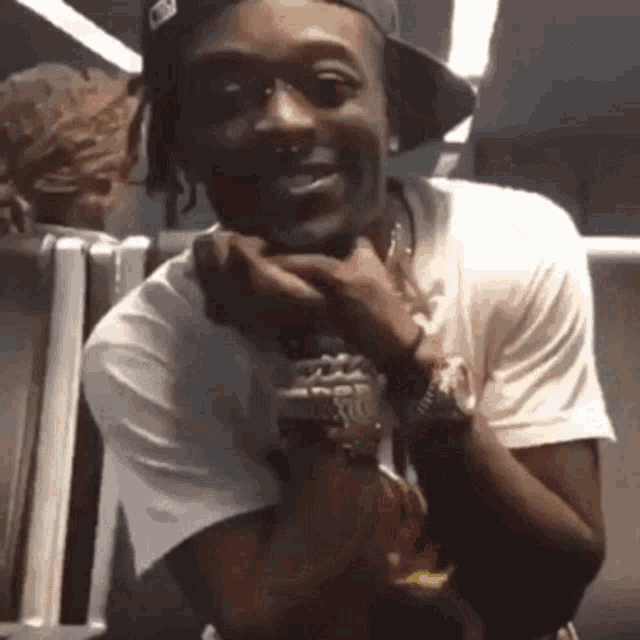 a man wearing a hat and a white shirt is smiling with his hands on his face .