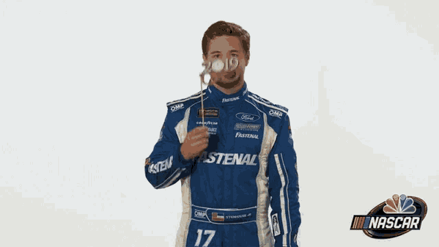a man in a blue and white fastenal racing suit is wearing a headband and glasses .