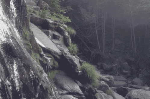 a waterfall is surrounded by rocks in the woods