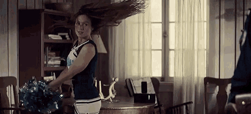 a cheerleader is dancing in a living room while holding pom poms .