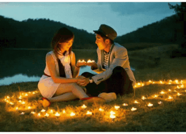 a man and a woman are sitting in the grass with lit candles