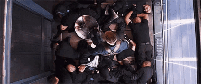 a group of people are laying on the floor in an elevator and one of them is holding a shield