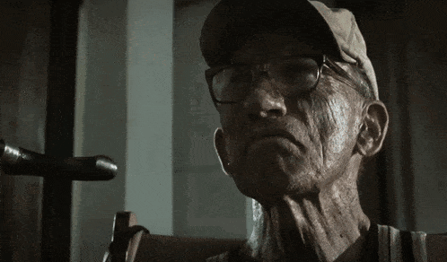 an elderly man wearing glasses and a hat looks at the camera