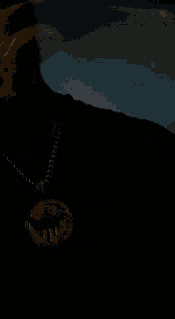 a man wearing a hat and a necklace is taking a selfie in a dark room .