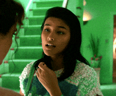 a woman in a green sweater talks to another woman in front of green stairs