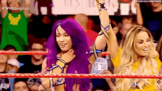 a couple of women standing in a wrestling ring with their arms in the air .